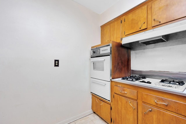 kitchen featuring brown cabinets, a warming drawer, under cabinet range hood, and white stovetop