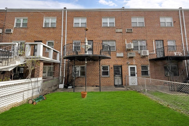 back of house with an AC wall unit, a lawn, fence, and brick siding