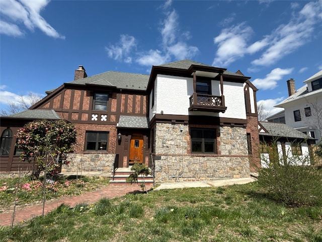view of front of property with stone siding, a chimney, stucco siding, a balcony, and roof with shingles