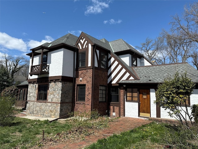 view of front facade with a shingled roof, brick siding, and a balcony