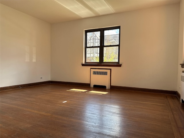 empty room with dark wood-type flooring, baseboards, and radiator