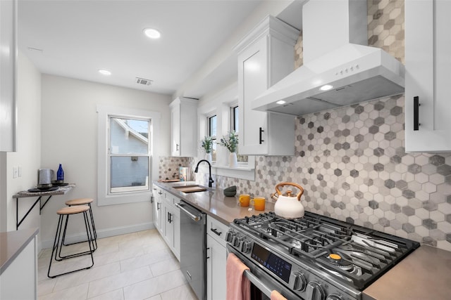 kitchen with wall chimney range hood, white cabinets, visible vents, a sink, and stainless steel appliances