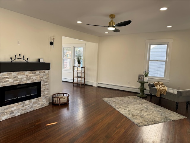living area with a fireplace, a baseboard heating unit, a ceiling fan, and wood finished floors