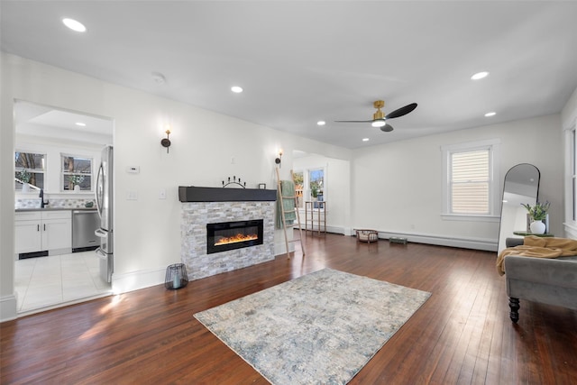 living room featuring ceiling fan, a fireplace, recessed lighting, wood-type flooring, and a baseboard heating unit