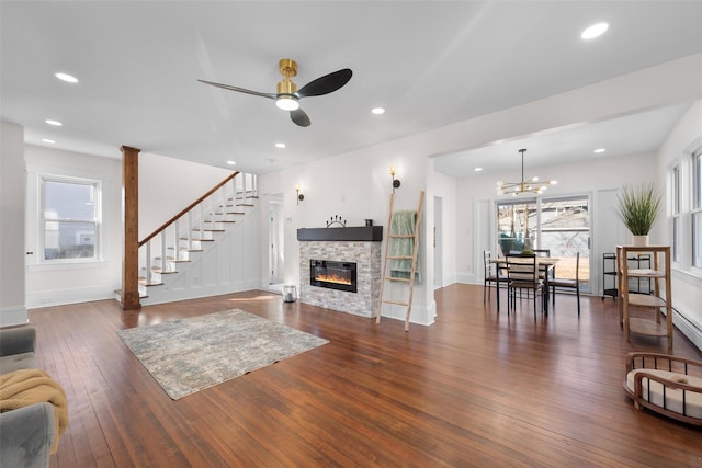 living area featuring ceiling fan with notable chandelier, a wealth of natural light, a stone fireplace, and hardwood / wood-style flooring
