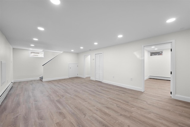 finished below grade area featuring baseboard heating, baseboards, recessed lighting, stairs, and light wood finished floors