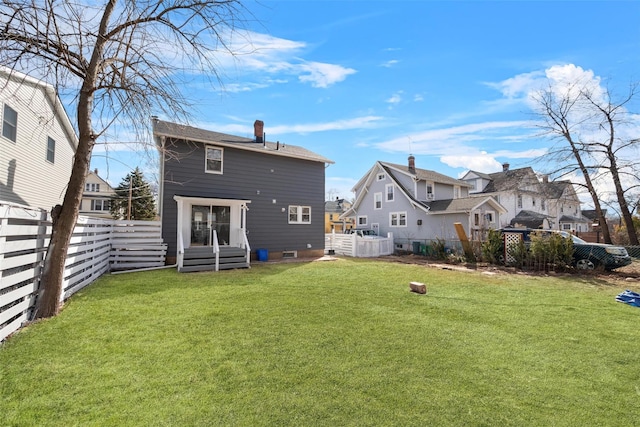 rear view of property featuring a yard, a fenced backyard, a residential view, and a chimney