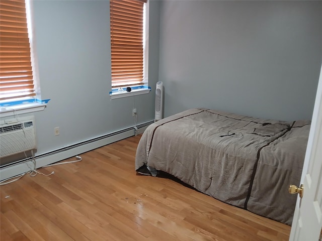 bedroom with a baseboard radiator, wood finished floors, and multiple windows