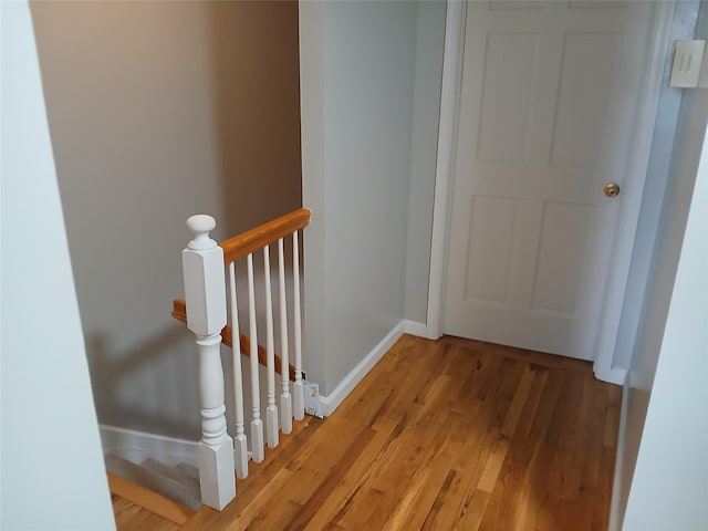 hall featuring light wood-style floors, baseboards, and an upstairs landing