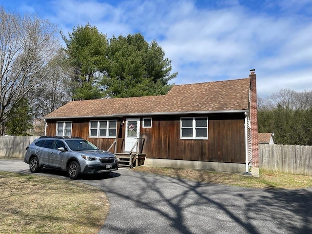 view of front of property featuring a chimney, driveway, entry steps, fence, and a shingled roof