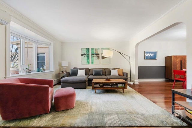living room featuring arched walkways, baseboards, wood finished floors, a wall mounted AC, and ornamental molding