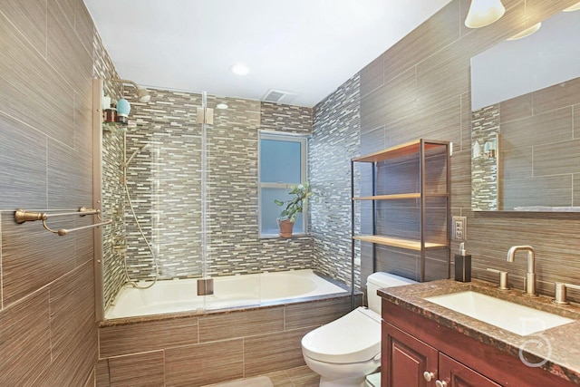 full bath with toilet, vanity, tiled shower / bath combo, and tile walls