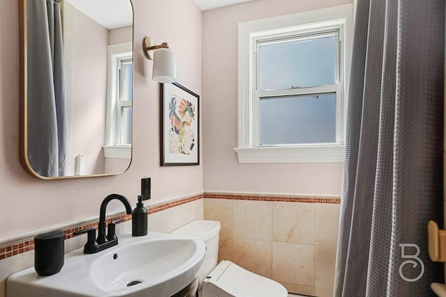bathroom featuring a wainscoted wall, toilet, a sink, tile walls, and a shower with shower curtain