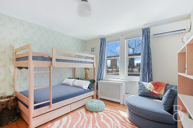 bedroom featuring wallpapered walls, radiator heating unit, a wall unit AC, and wood finished floors