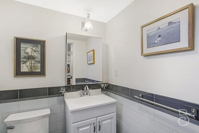 bathroom featuring wainscoting, toilet, vanity, and tile walls