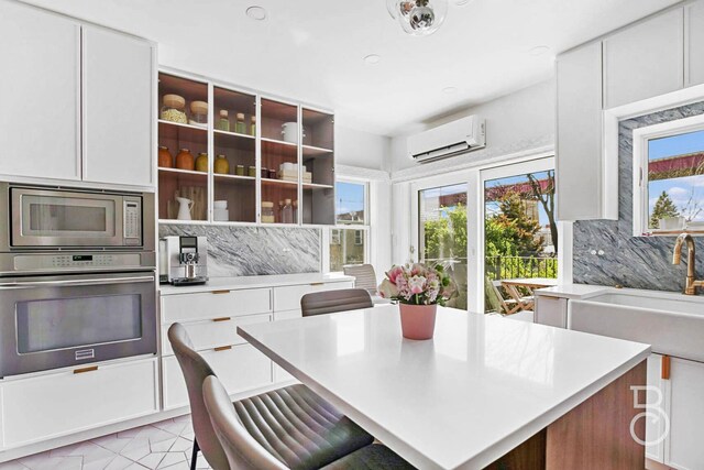 kitchen featuring a wall unit AC, white cabinets, appliances with stainless steel finishes, light countertops, and backsplash