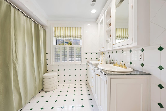 full bathroom with visible vents, a sink, double vanity, and tile walls