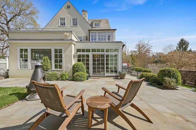 rear view of property featuring a chimney, a patio area, and stucco siding