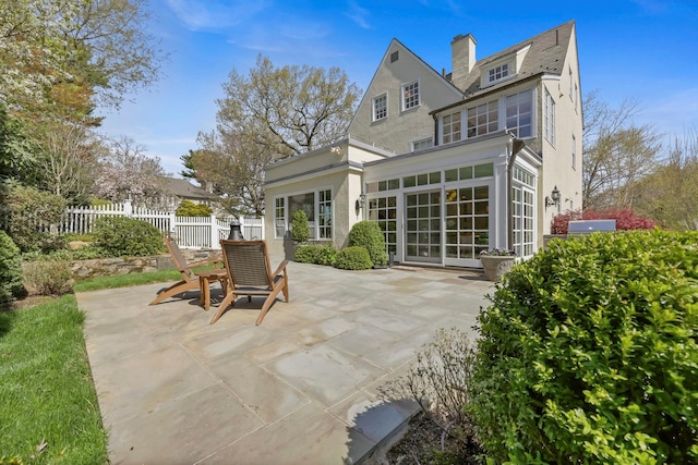rear view of house featuring a patio, fence, a chimney, and stucco siding