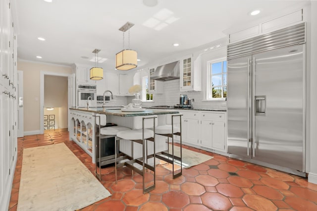 kitchen featuring wall chimney range hood, backsplash, white cabinets, and stainless steel built in fridge