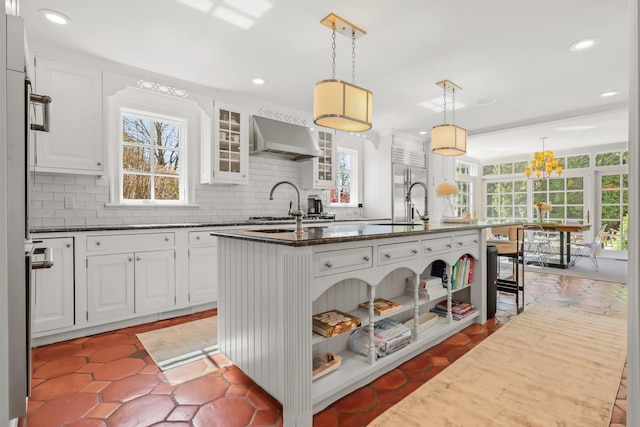 kitchen featuring wall chimney range hood, plenty of natural light, and a kitchen island with sink