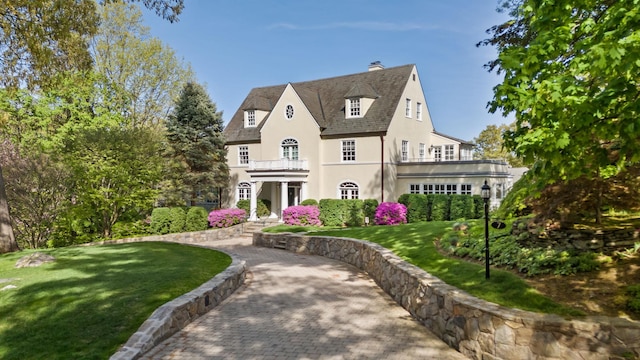 view of front facade with a chimney, a front lawn, a balcony, and stucco siding