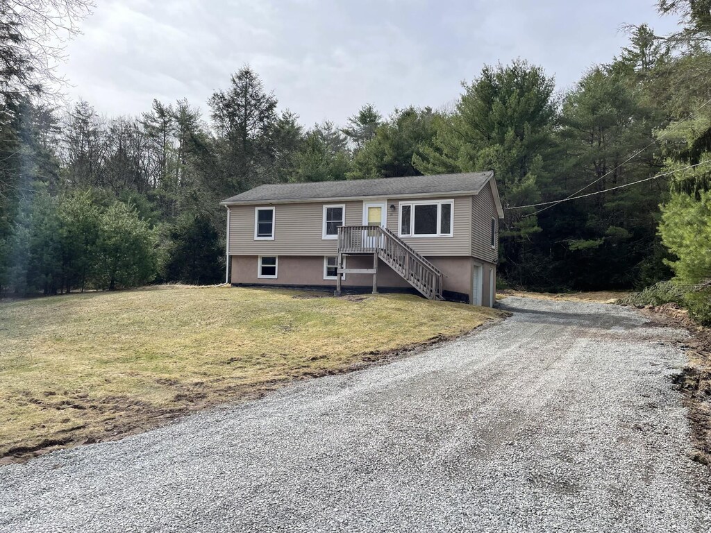 bi-level home with a garage, gravel driveway, and a front lawn
