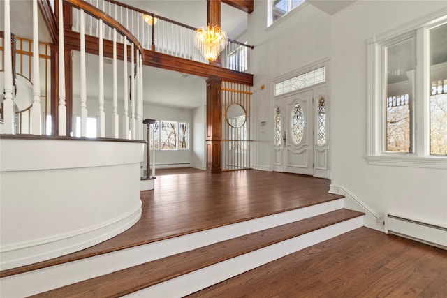 entrance foyer with stairway, a chandelier, wood finished floors, a baseboard heating unit, and a high ceiling