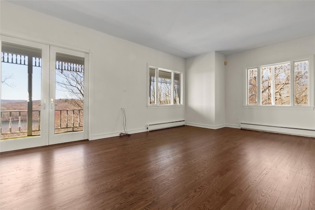 empty room featuring baseboard heating, baseboards, and dark wood finished floors