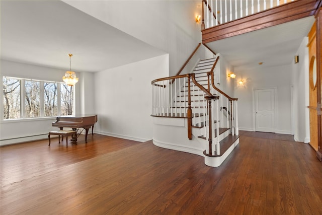foyer with stairway, baseboard heating, wood finished floors, an inviting chandelier, and baseboards