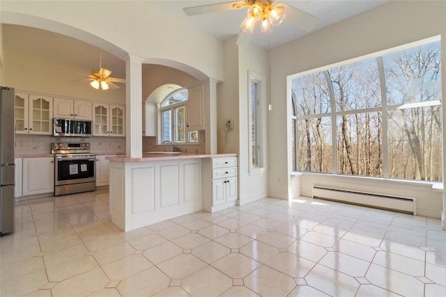 kitchen featuring baseboard heating, glass insert cabinets, ceiling fan, stainless steel appliances, and arched walkways