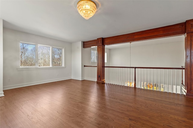 spare room with wood finished floors, a notable chandelier, and baseboards