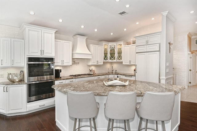 kitchen with visible vents, a sink, premium range hood, decorative backsplash, and appliances with stainless steel finishes
