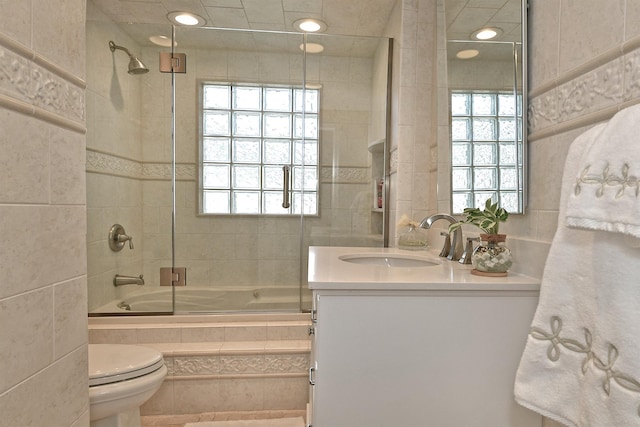 bathroom with tiled shower / bath, toilet, vanity, and tile walls