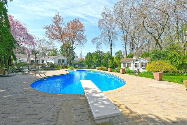 outdoor pool with an outdoor structure, a patio area, fence, and a diving board