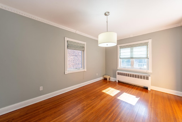 spare room with radiator heating unit, wood-type flooring, baseboards, and crown molding