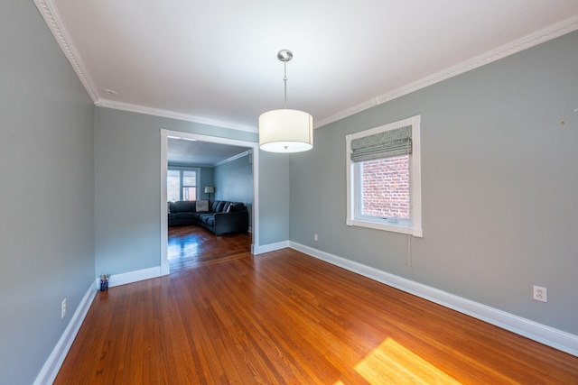 empty room featuring crown molding, wood finished floors, and baseboards