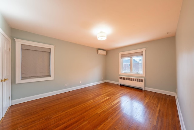 unfurnished room featuring baseboards, a wall unit AC, radiator, and wood finished floors