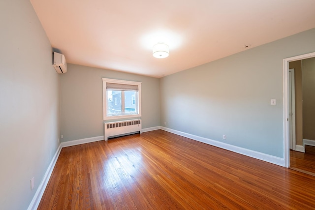 unfurnished room featuring a wall unit AC, radiator heating unit, baseboards, and wood finished floors