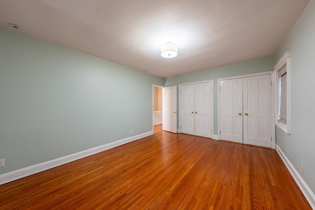 unfurnished bedroom featuring baseboards, two closets, and wood finished floors