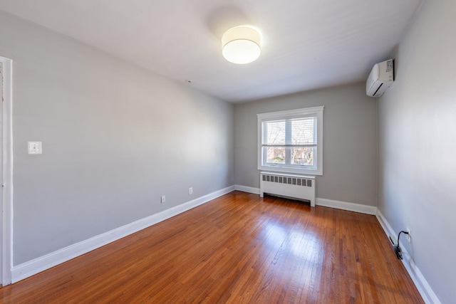 unfurnished room featuring radiator heating unit, hardwood / wood-style floors, baseboards, and a wall unit AC