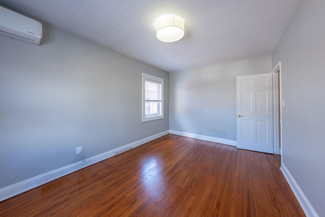 spare room featuring a wall mounted AC, dark wood-type flooring, and baseboards