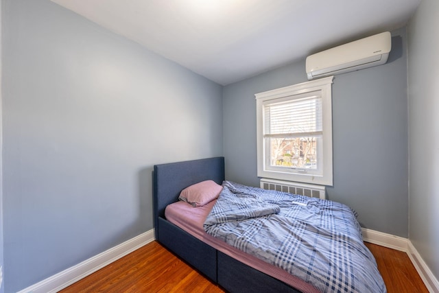 bedroom with a wall unit AC, wood finished floors, and baseboards