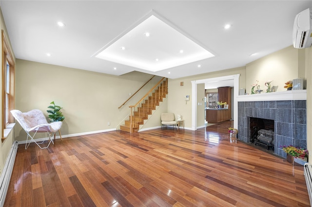 living room with baseboards, a wall mounted AC, stairway, wood finished floors, and a baseboard heating unit