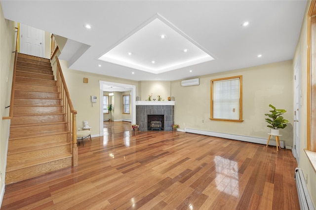 unfurnished living room featuring a raised ceiling, a baseboard radiator, a wall unit AC, and stairway