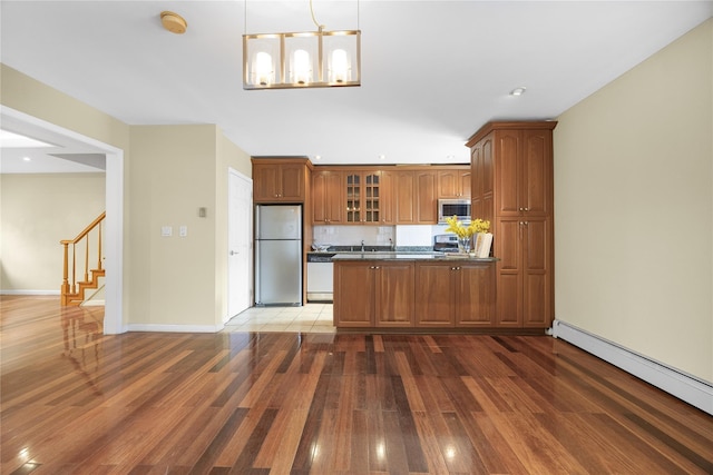kitchen featuring baseboard heating, glass insert cabinets, dark countertops, brown cabinets, and stainless steel appliances