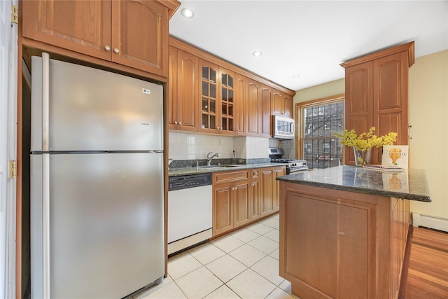 kitchen featuring dark stone countertops, glass insert cabinets, a sink, appliances with stainless steel finishes, and decorative backsplash