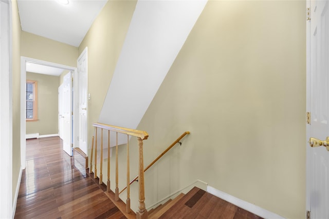hall featuring dark wood-style flooring, baseboards, and an upstairs landing