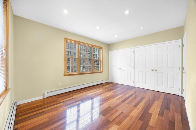 unfurnished bedroom with a baseboard heating unit, a baseboard radiator, multiple closets, and wood finished floors