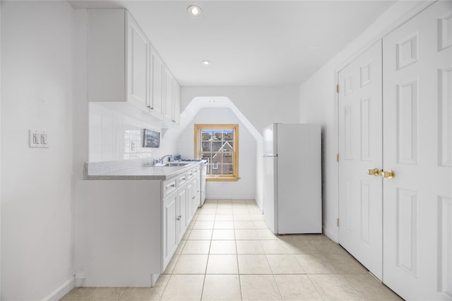 kitchen with light tile patterned floors, light countertops, freestanding refrigerator, white cabinets, and a sink